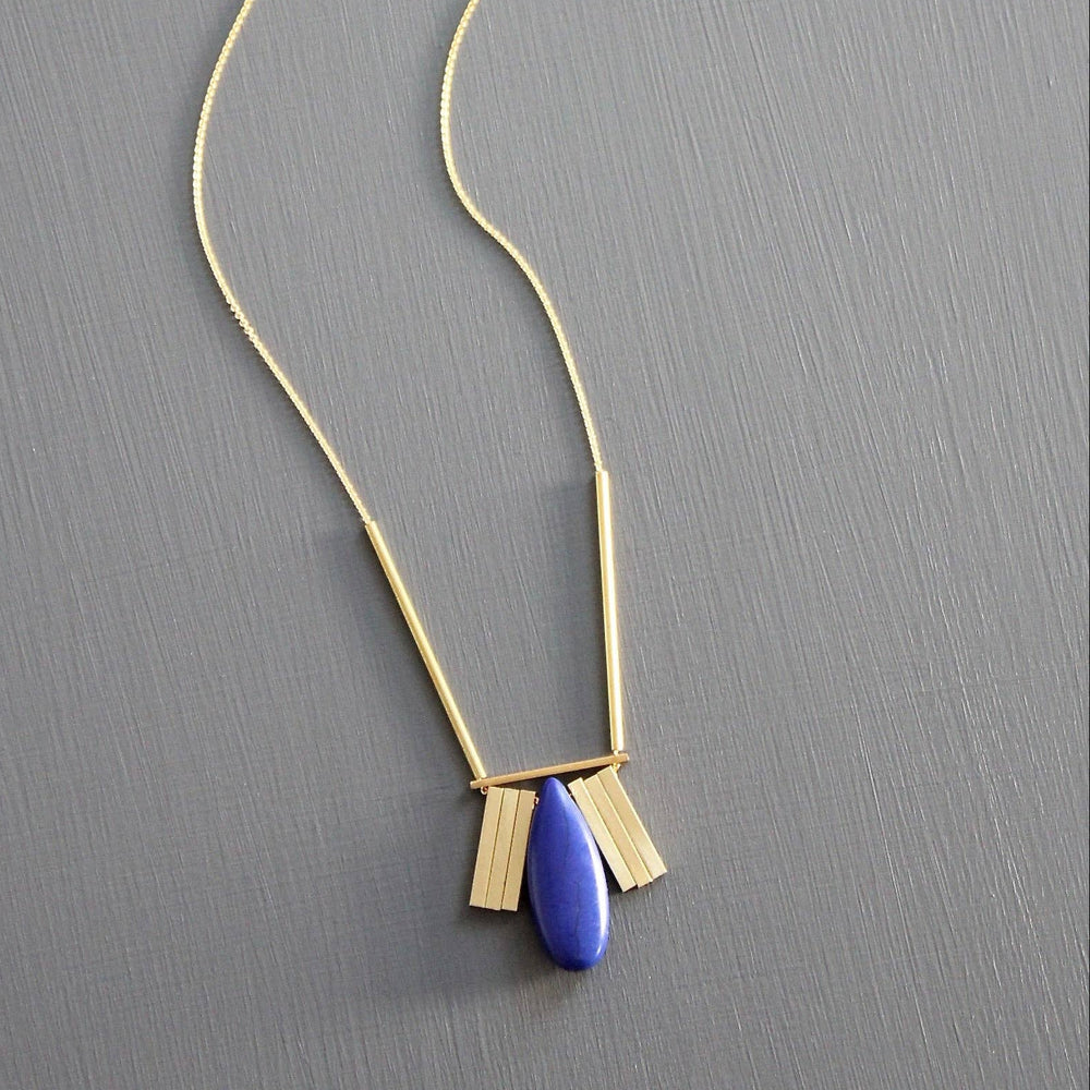 Gold necklace with a blue pendant on a gray background