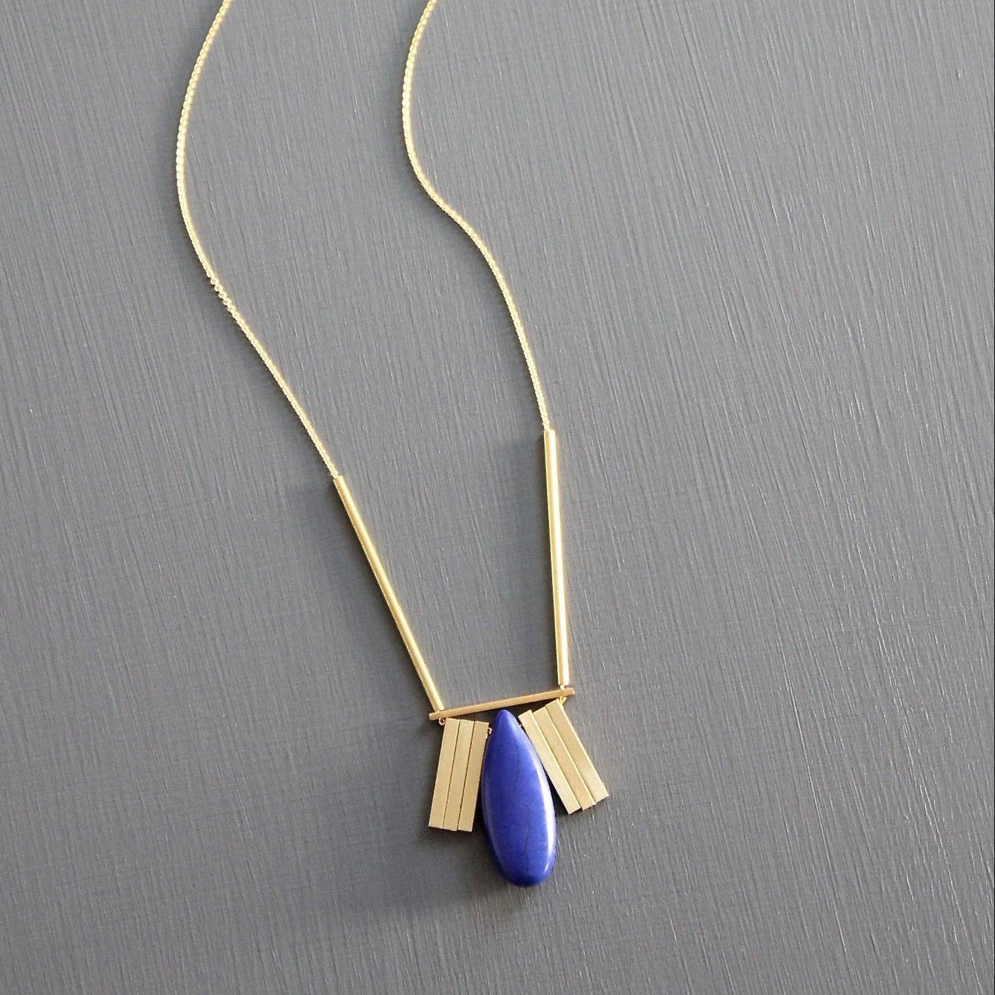 Gold necklace with a blue pendant on a gray background