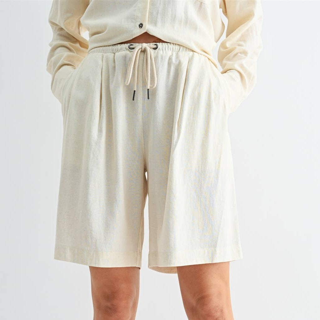 Person wearing cream shorts and a matching top on a white background