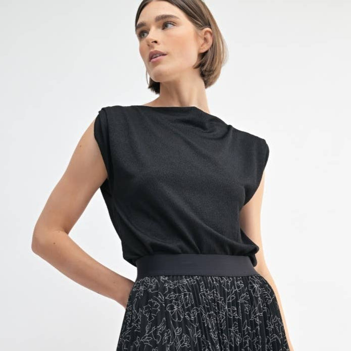 Woman wearing a black sleeveless top with a draped design on a white background