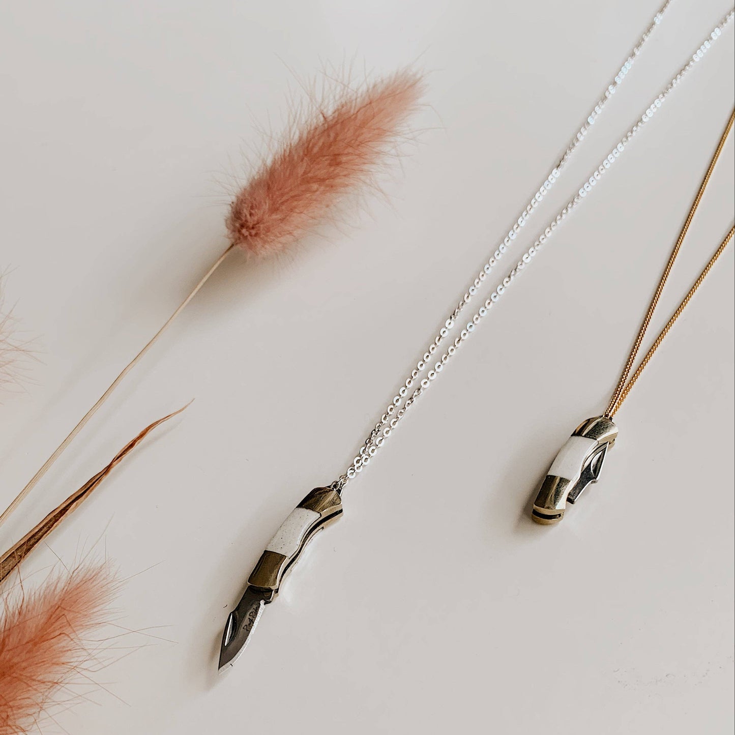 Two necklaces on a light surface with dried grasses
