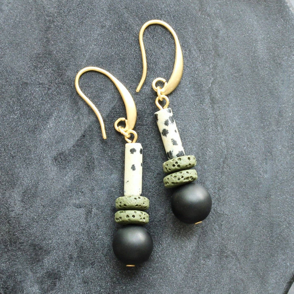 Pair of earrings with black beads and gold accents on a gray stone surface