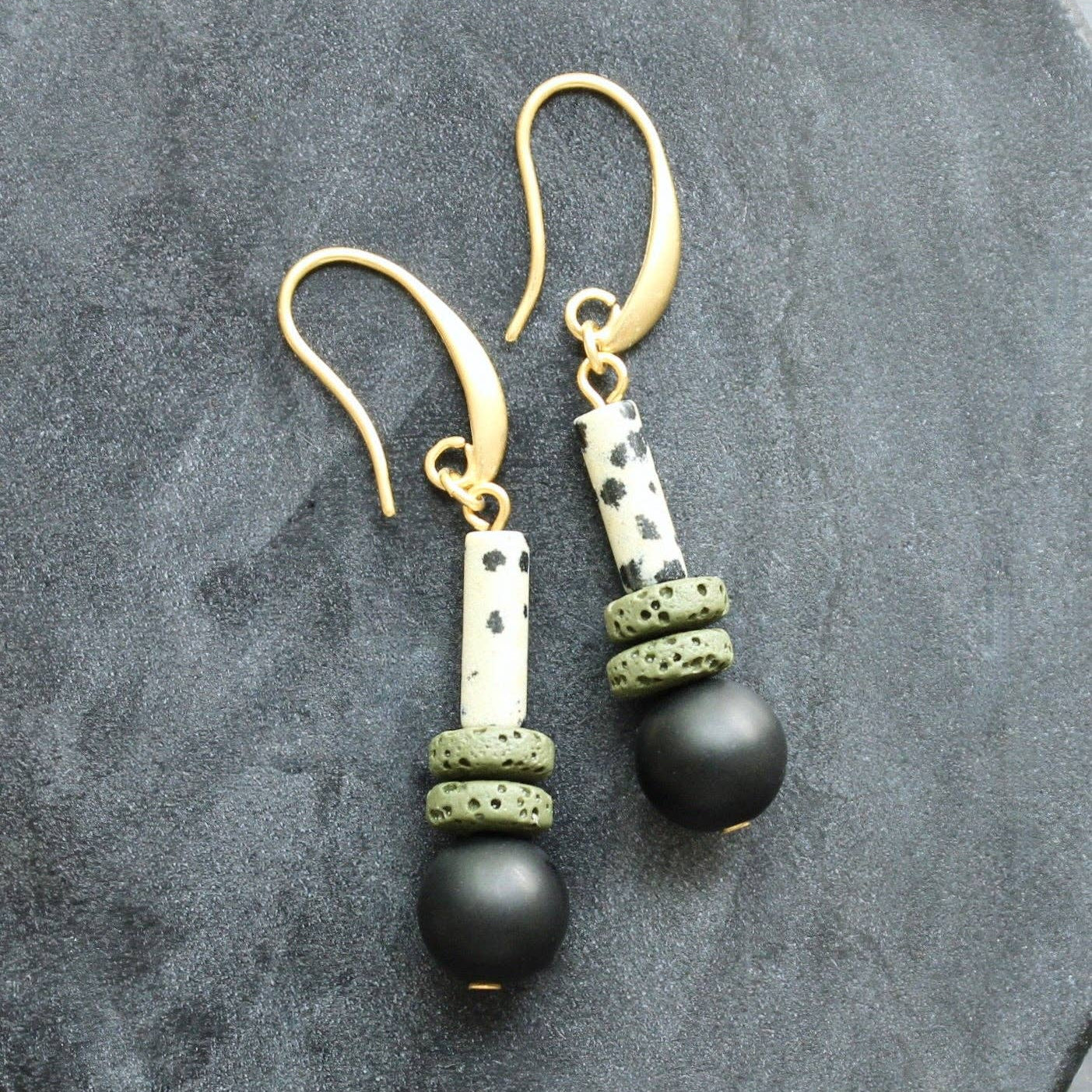 Pair of earrings with black beads and gold accents on a gray stone surface