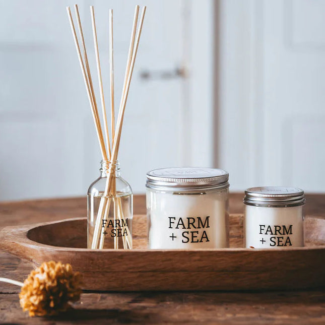 Candle and diffuser set on a wooden tray with 'Farm + Sea' branding against a light background.