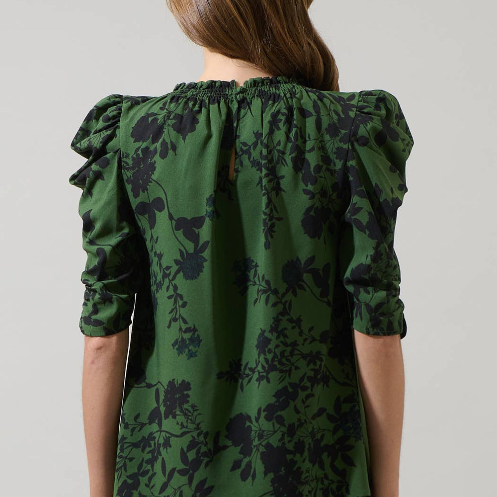 Woman wearing a green floral blouse with ruffled sleeves on a plain background