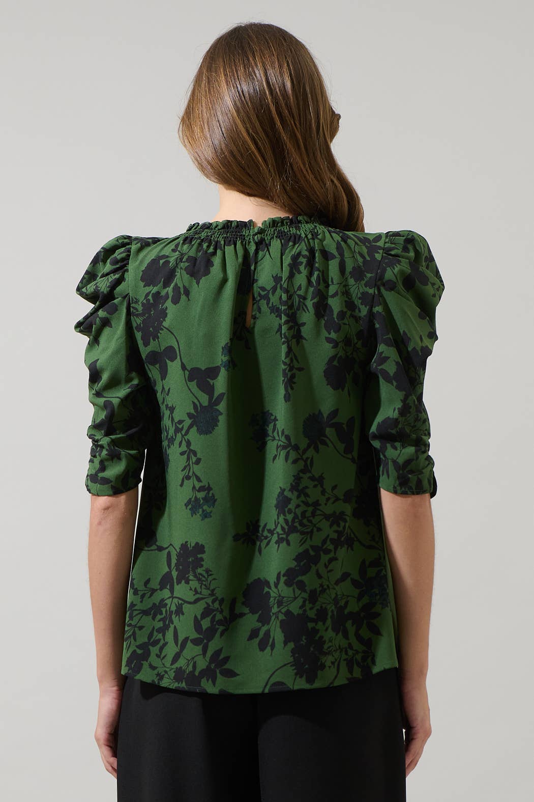 Woman wearing a green floral blouse with ruffled sleeves on a plain background