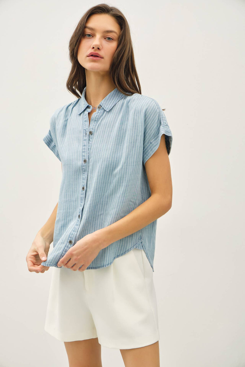 Woman wearing a light blue striped sleeveless shirt and white shorts on a plain background