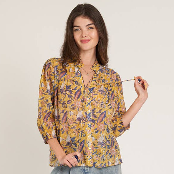 Woman wearing a floral blouse and light blue pants on a plain background
