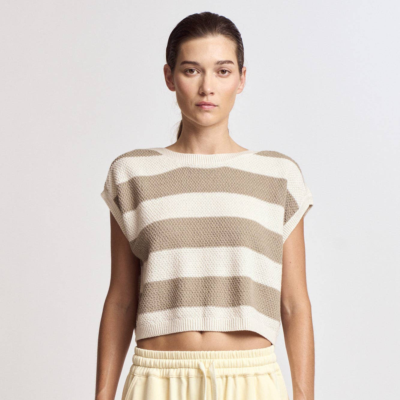 Woman wearing a striped sleeveless top and beige pants on a plain background