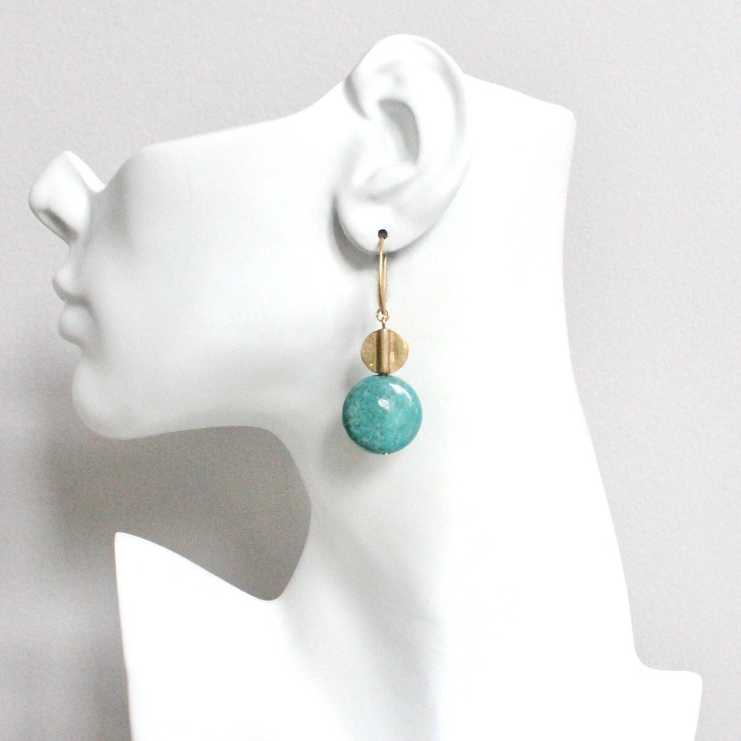 Turquoise earrings on a white mannequin head against a gray background