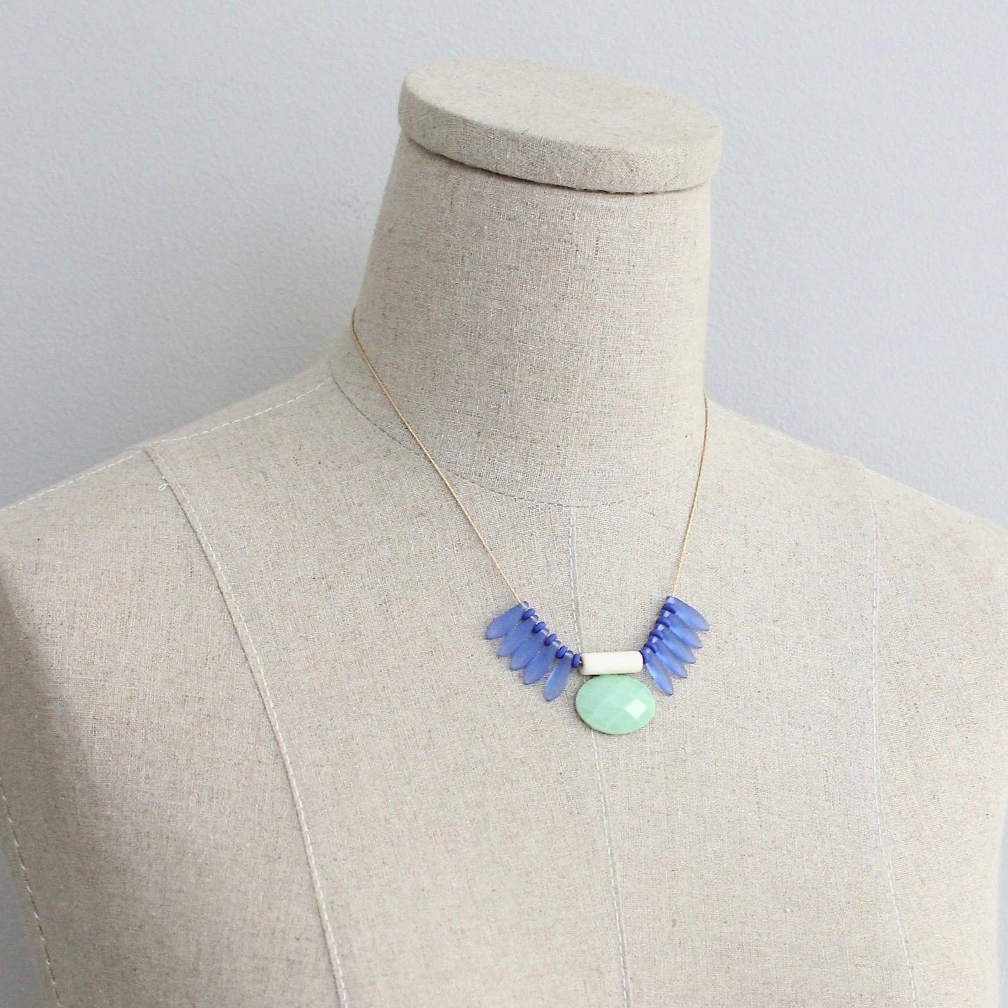 Necklace with blue and green beads on a mannequin against a plain background