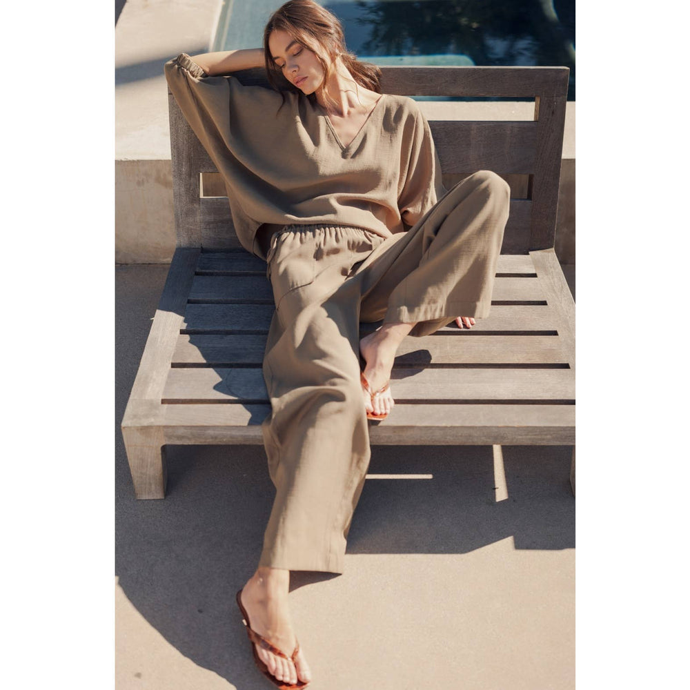 
                      
                        Woman in beige outfit sitting on a wooden bench by a poolside
                      
                    