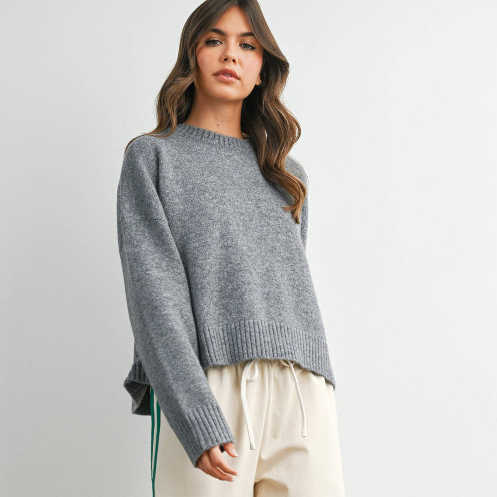 Woman wearing a gray sweater and cream pants with green stripes on a white background