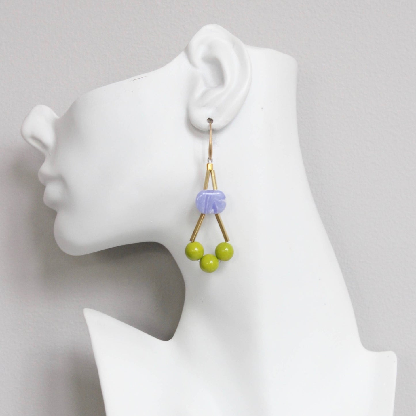 Earrings with green beads on a mannequin ear against a gray background