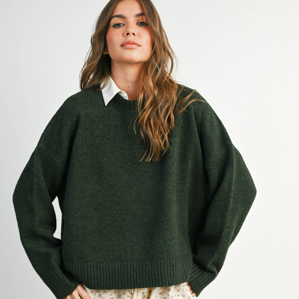 
                      
                        Woman wearing a green sweater and patterned pants on a plain background
                      
                    