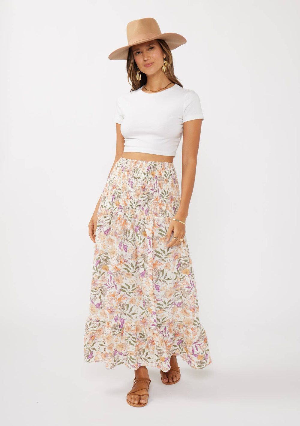 Woman wearing a white crop top and floral skirt with a hat on a white background