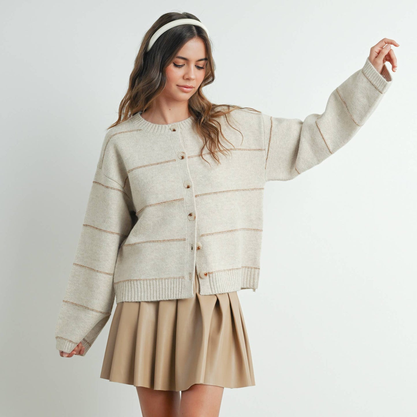 Woman wearing a beige sweater and skirt with white sneakers on a plain background