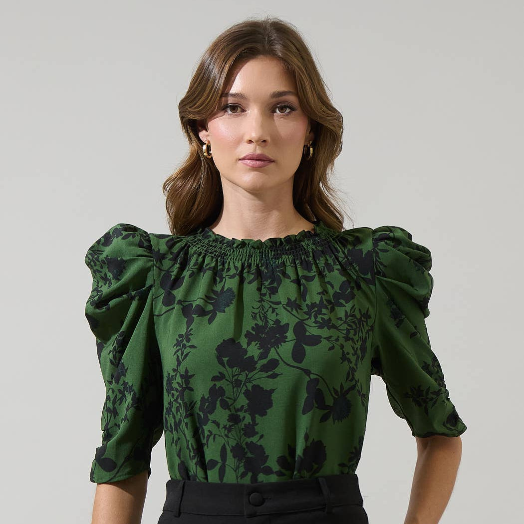Woman wearing a green floral blouse with puff sleeves against a gray background