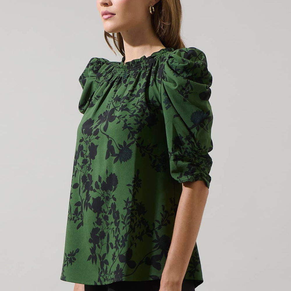 
                      
                        Woman wearing a green floral blouse against a gray background
                      
                    