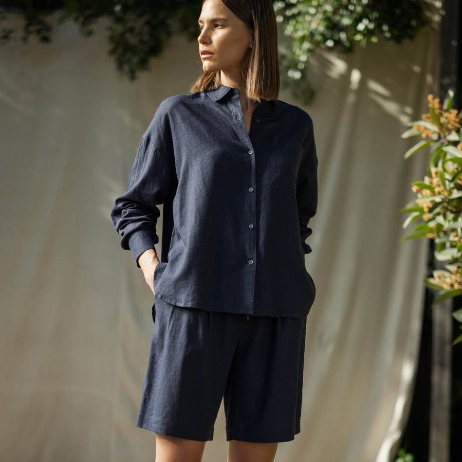 Woman wearing a navy blue shirt and shorts standing on a wooden deck with greenery in the background