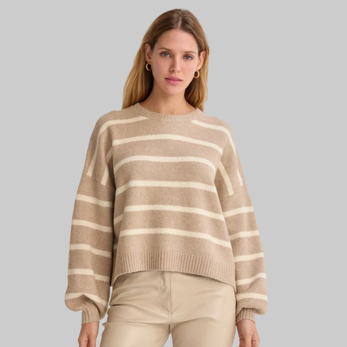 Woman wearing a beige and white striped sweater and pants on a plain background