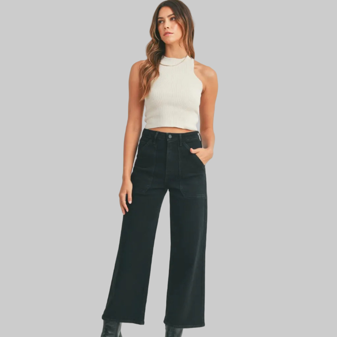 Woman wearing a white sleeveless top and black high-waisted jeans on a white background