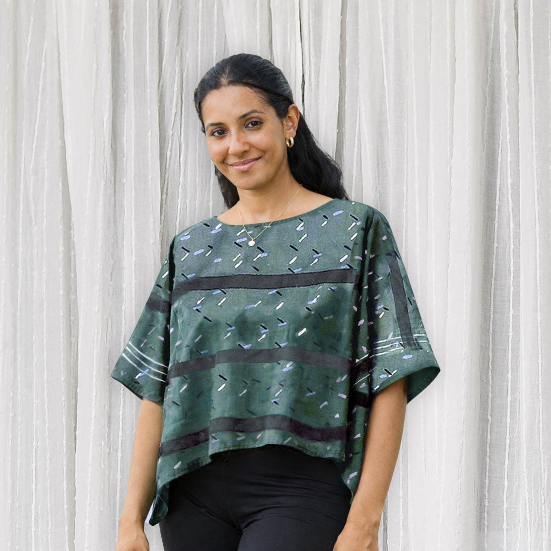 Woman wearing a green patterned blouse against a white curtain background