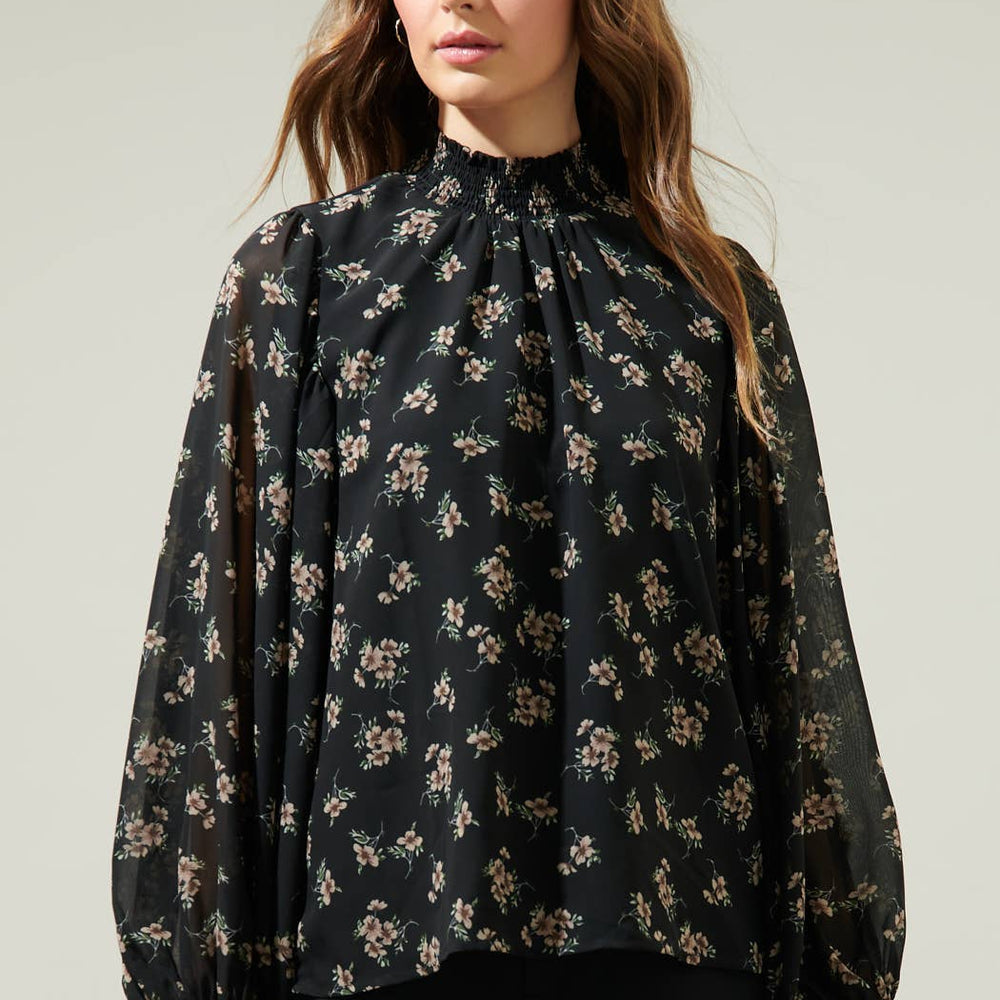
                      
                        Woman wearing a black floral blouse against a plain background
                      
                    