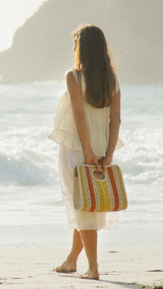 Woman in white dress holding a colorful bag on a beach.