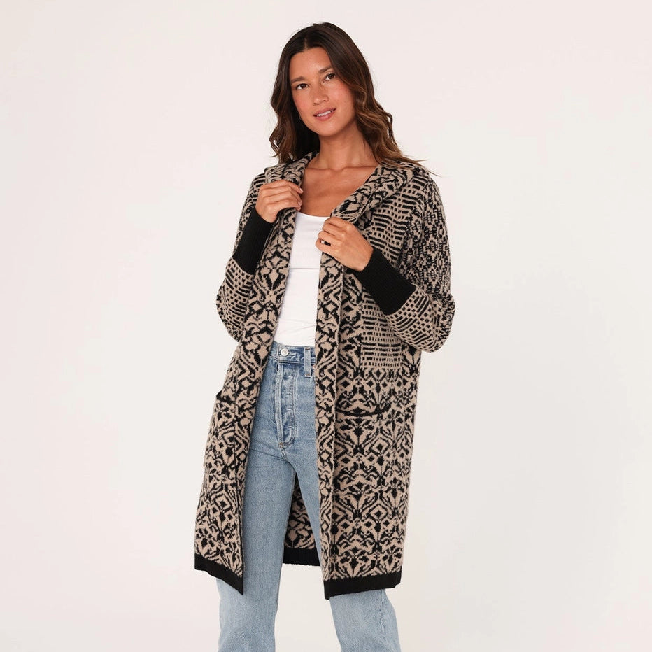 Woman wearing a patterned cardigan, white shirt, and light blue jeans on a white background